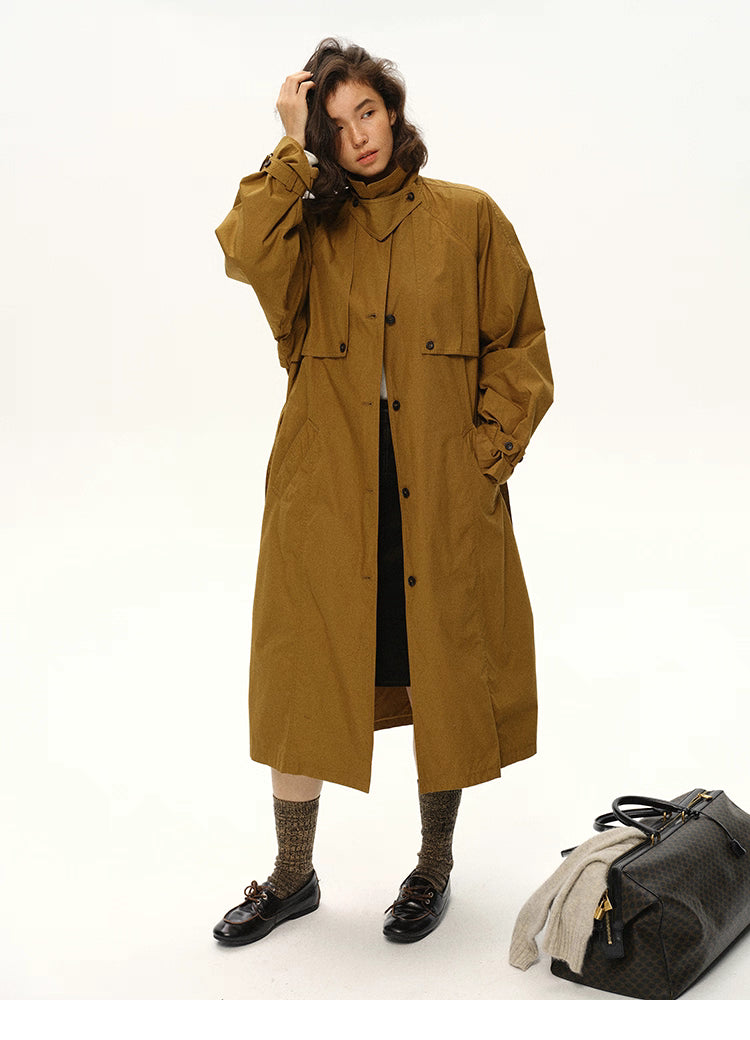 Woman posing in a maple brown long trench coat with one hand in hair.