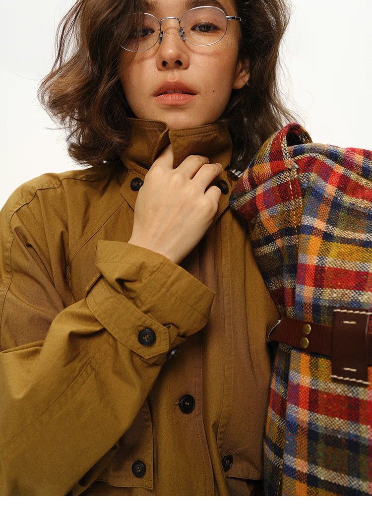 Close-up of woman holding trench coat collar while carrying a plaid bag.