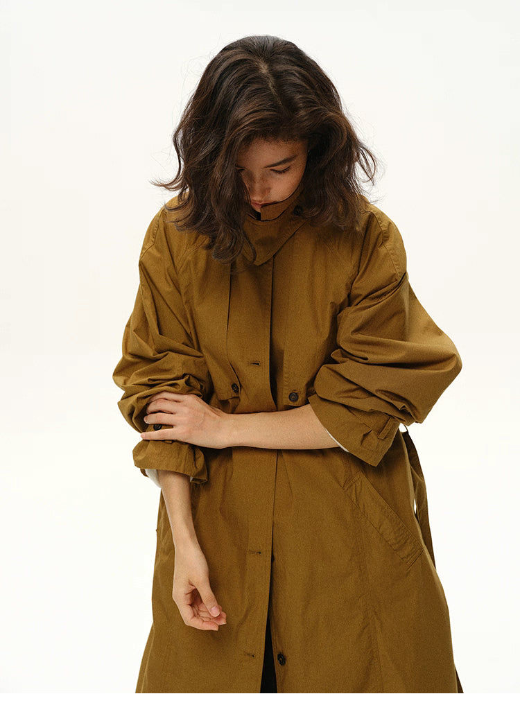 Woman rolling up sleeves of a maple brown long trench coat.