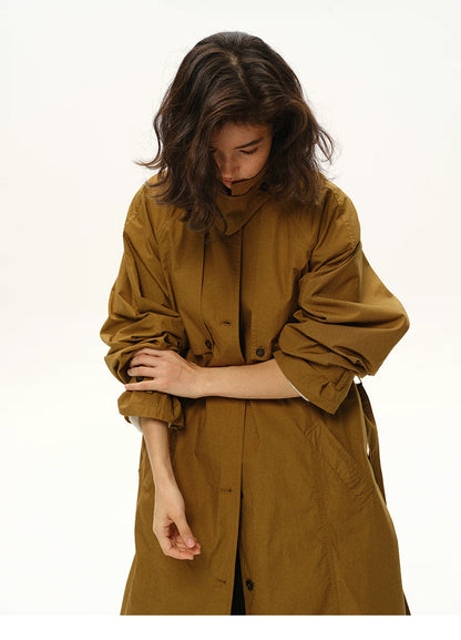 Woman rolling up sleeves of a maple brown long trench coat.