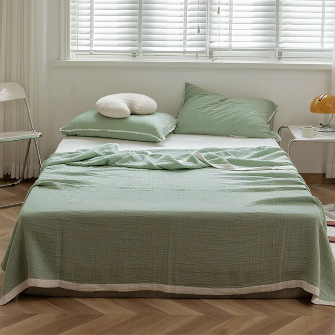 Bean green triple layer ripple gauze cotton quilt with zigzag edge draped on bed in bright minimalist bedroom.