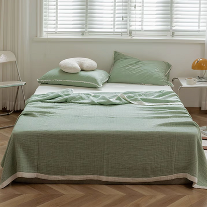 Bean green triple layer ripple gauze cotton quilt with zigzag edge draped on bed in bright minimalist bedroom.