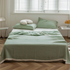 Bean green triple layer ripple gauze cotton quilt with zigzag edge draped on bed in bright minimalist bedroom.
