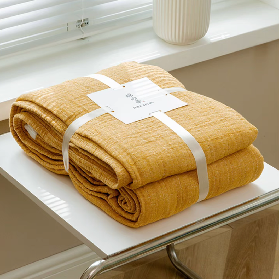 Bright yellow triple layer gauze cotton quilt neatly folded and tied with label on white table.