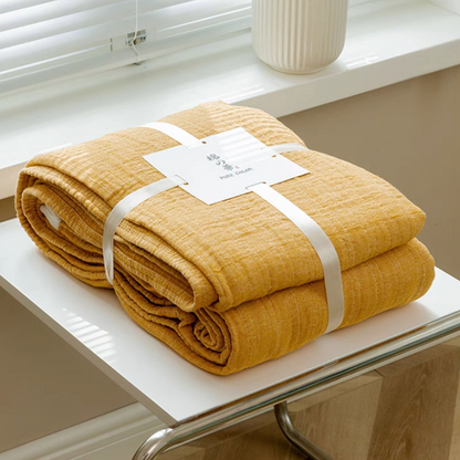 Bright yellow triple layer gauze cotton quilt neatly folded and tied with label on white table.
