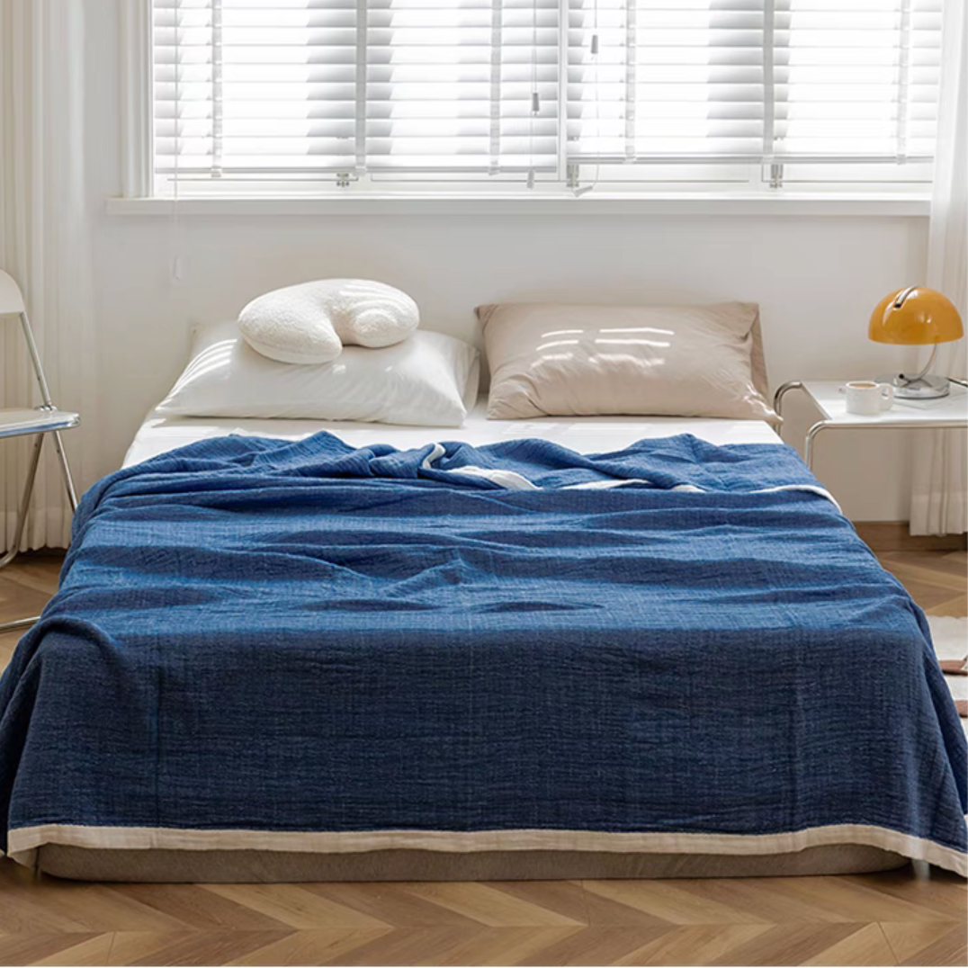 Dark blue ripple gauze cotton quilt with zigzag edge styled on minimalist bedroom bed.