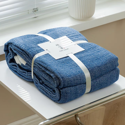 Dark blue ripple gauze cotton quilt folded and secured with label on modern side table.