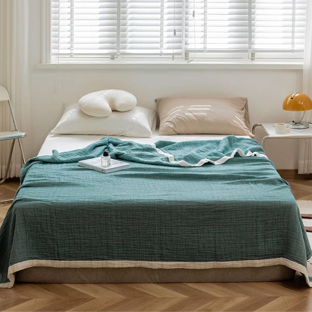 Dark green ripple gauze cotton quilt with zigzag edge draped over bed in bright modern bedroom.