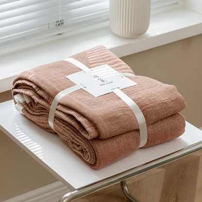 Deep pink triple layer gauze cotton quilt neatly folded and tied with product label on white table.