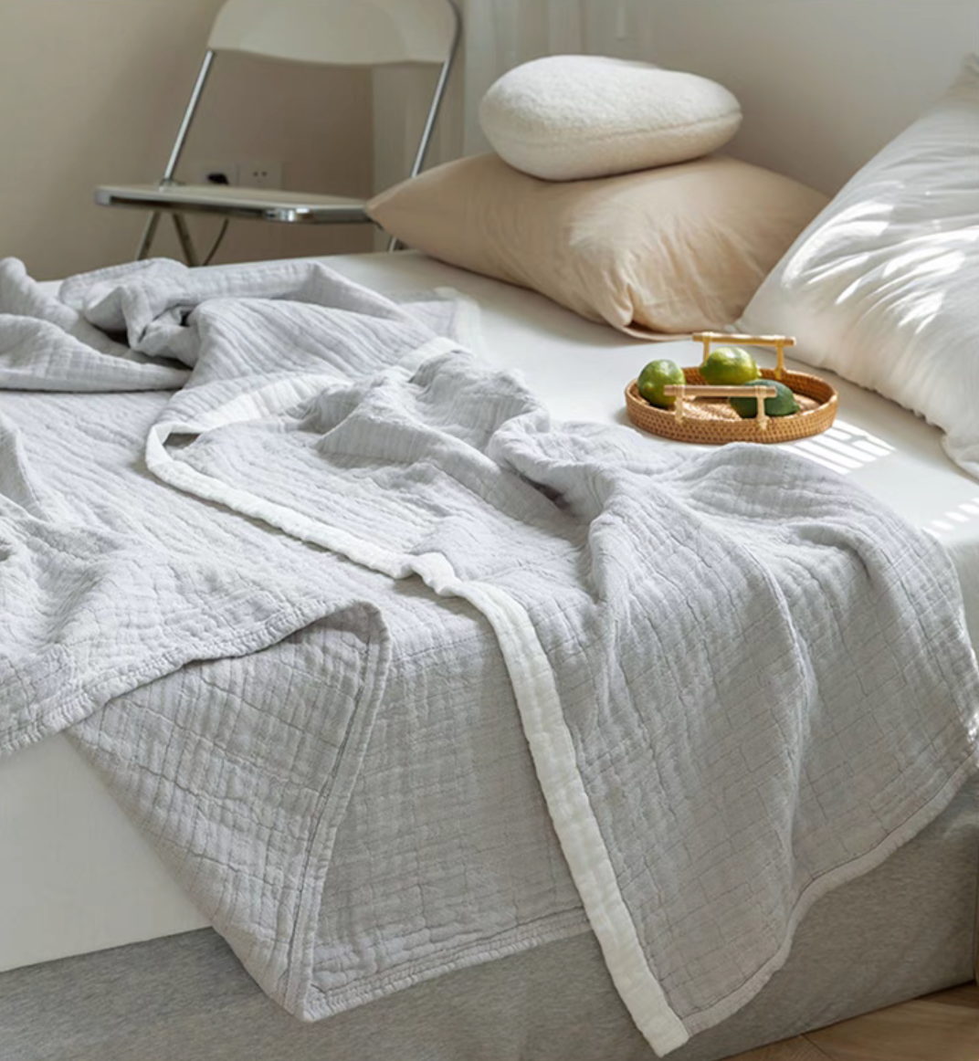 Light gray triple layer ripple gauze cotton quilt draped casually over bed with decorative tray.