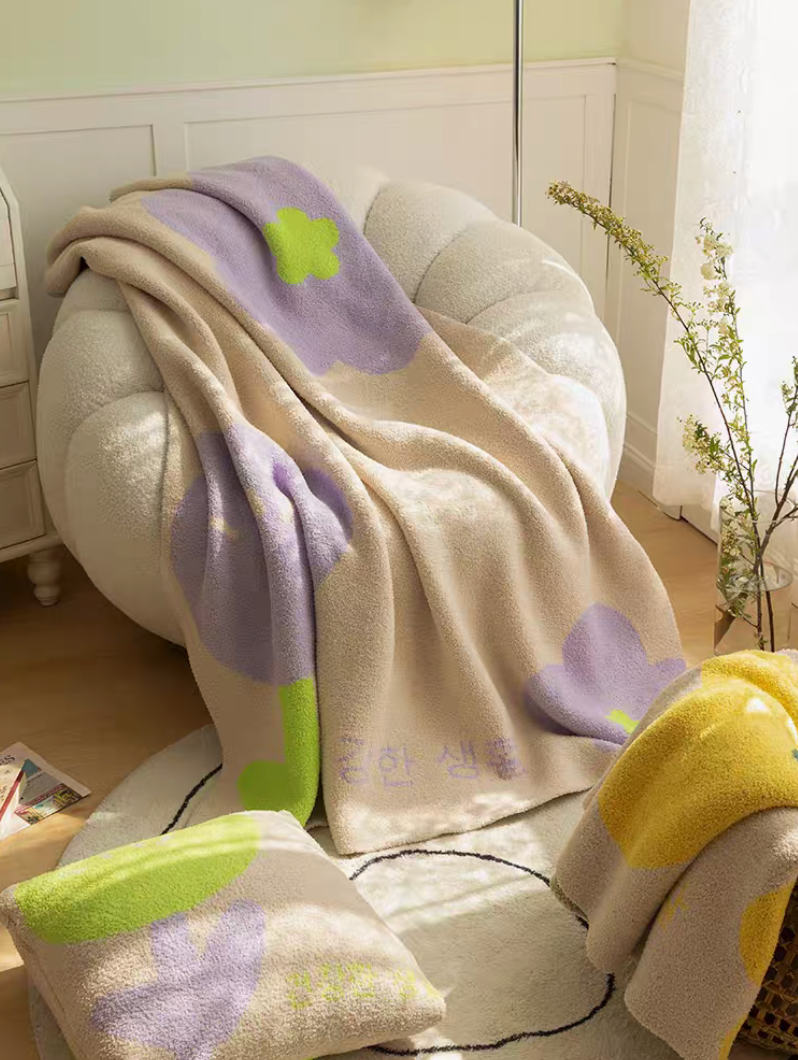 Tulip Luxe Blanket in tulip purple draped over a cream armchair with matching pillow and soft sunlight living room setting