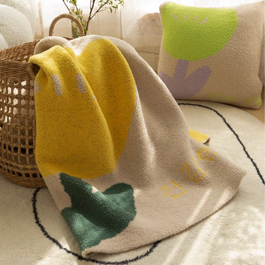 Tulip Luxe Blanket in tulip yellow styled over woven basket with matching pillow creating warm decorative home scene