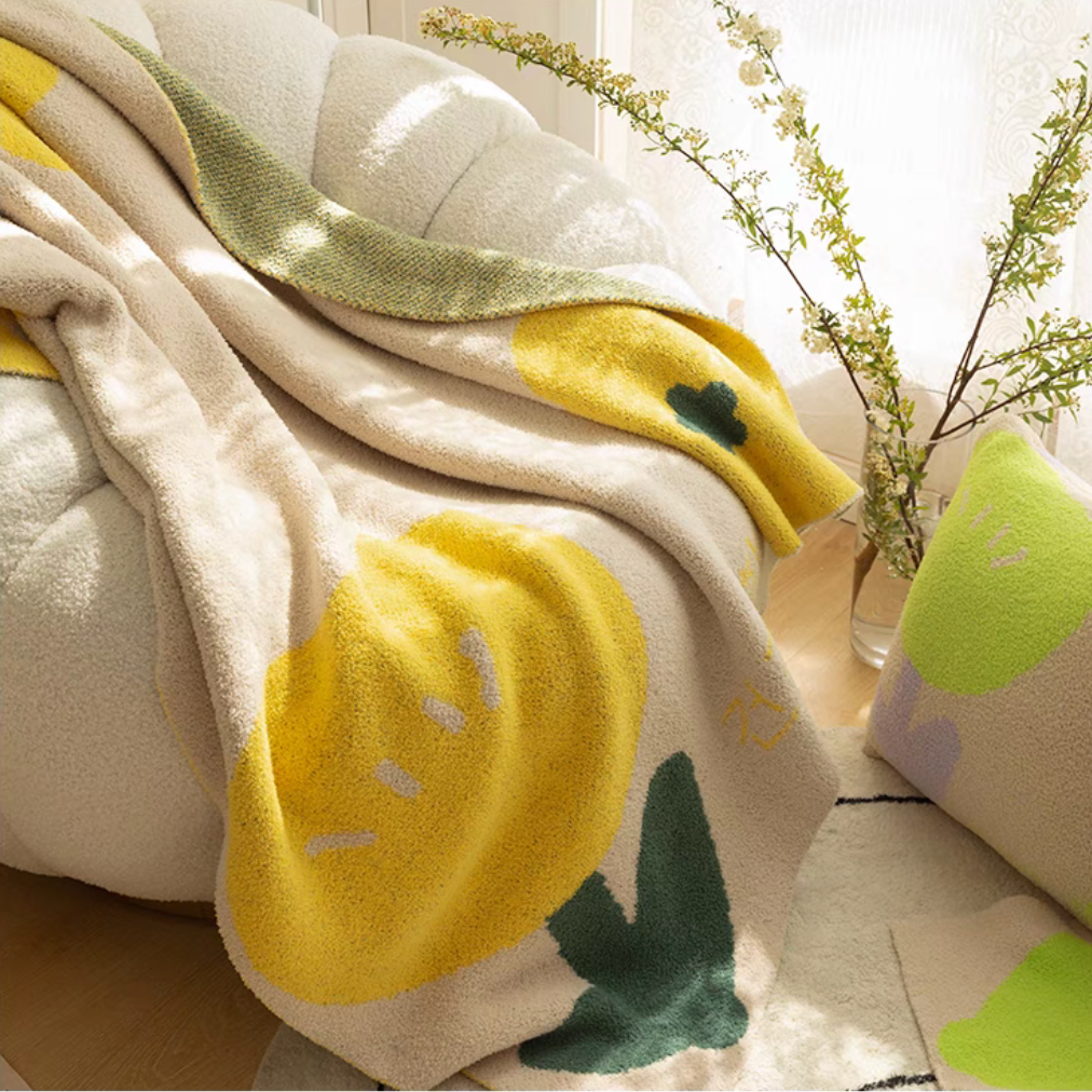 Tulip Luxe Blanket in tulip yellow draped over armchair with bright sunlight highlighting bold yellow tulip pattern
