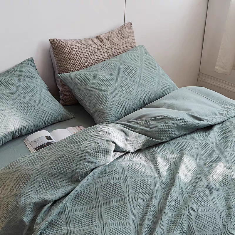 Greenish blue organic cotton waffle weave bedding set with matching pillow shams displayed in minimalist bedroom