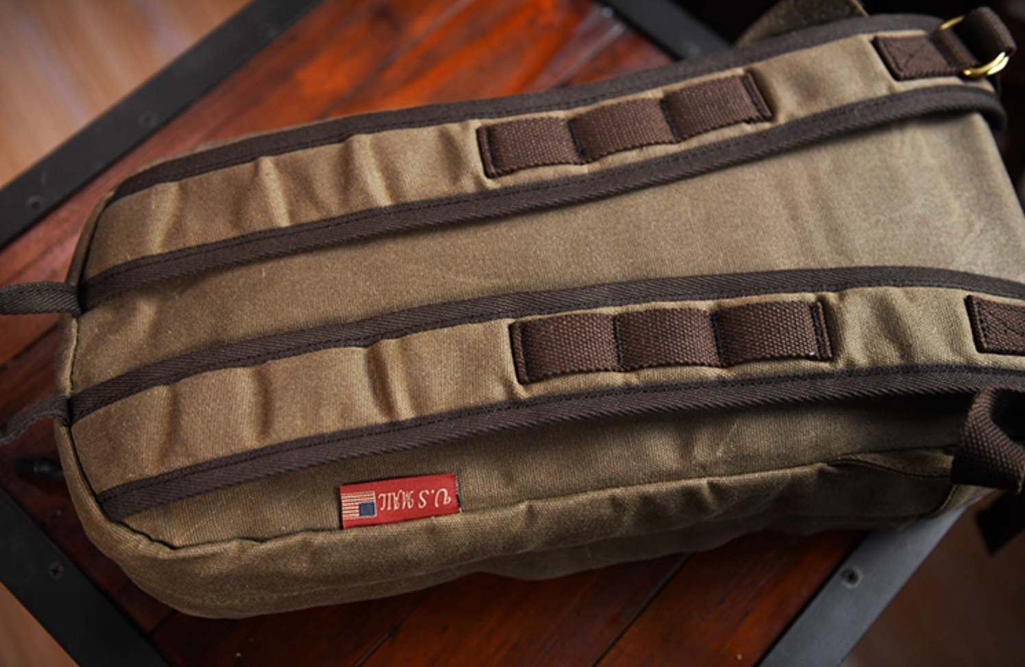 Back view of waxed canvas backpack showing padded straps and U.S. Mail tag label.