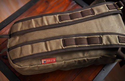 Back view of waxed canvas backpack showing padded straps and U.S. Mail tag label.