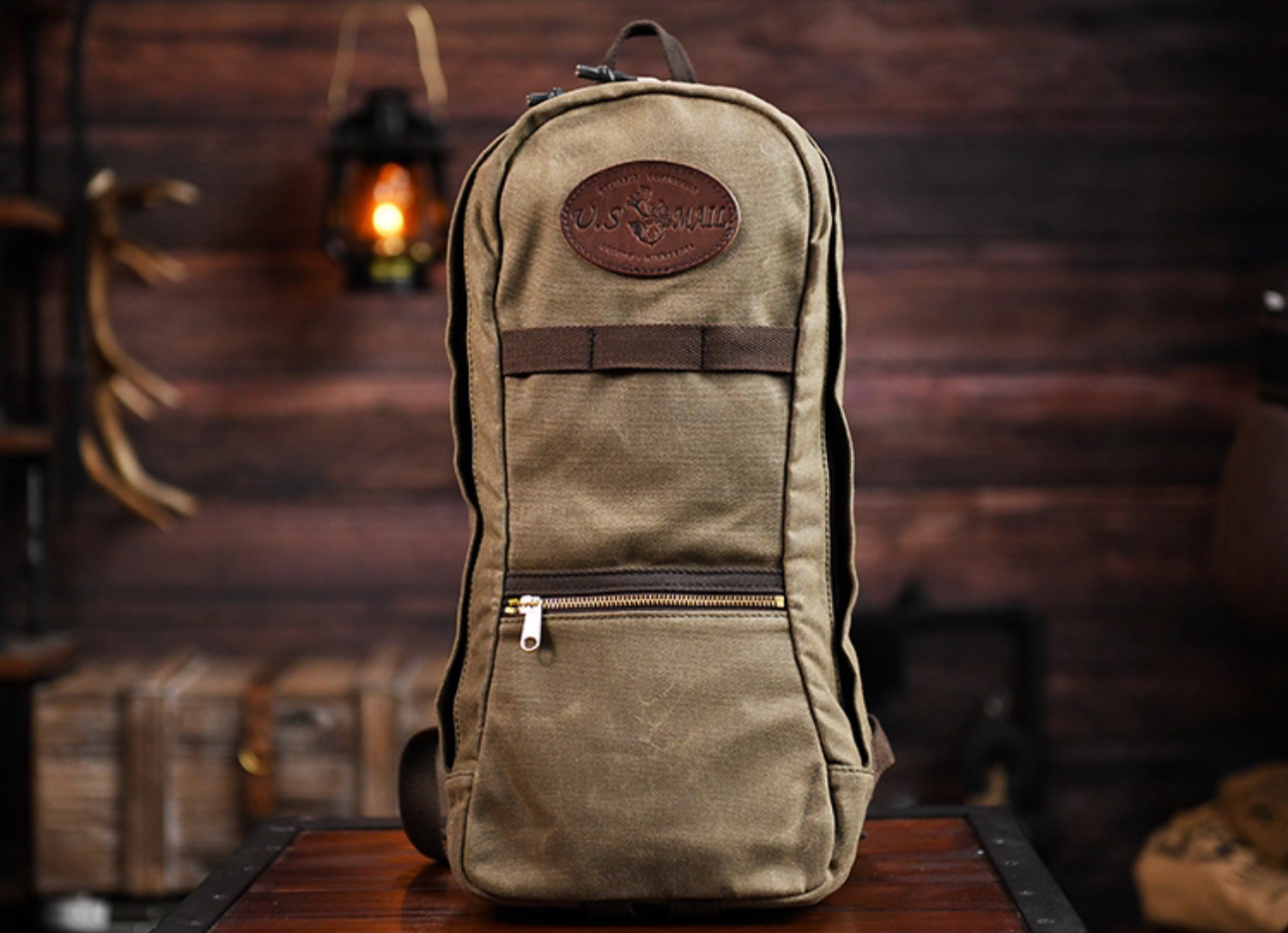 Front view of U.S. Mail waxed canvas backpack in army green with leather patch and front zipper.