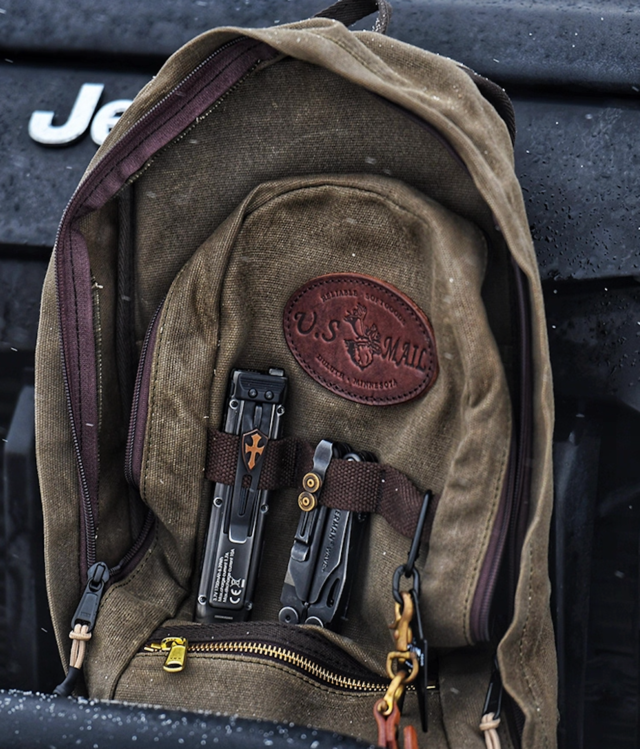 U.S. Mail waxed canvas backpack resting on Jeep with multitools attached to front straps.