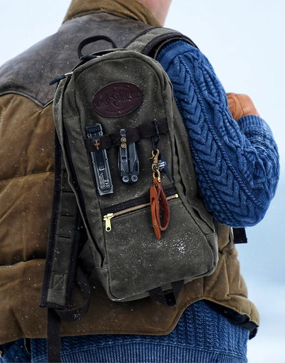 Man wearing U.S. Mail waxed canvas backpack outdoors in snowy weather with brown vest and blue sweater.