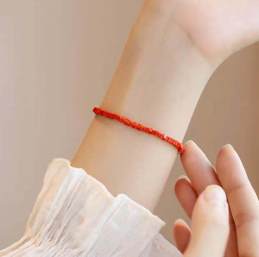Close-up of vermilion stone vintage bracelet worn on wrist with hand gently touching highlighting bright red tile bead texture