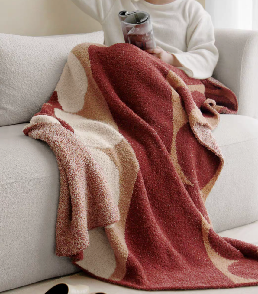 Red geometric circle throw blanket covering person sitting on sofa, demonstrating soft and cozy feel