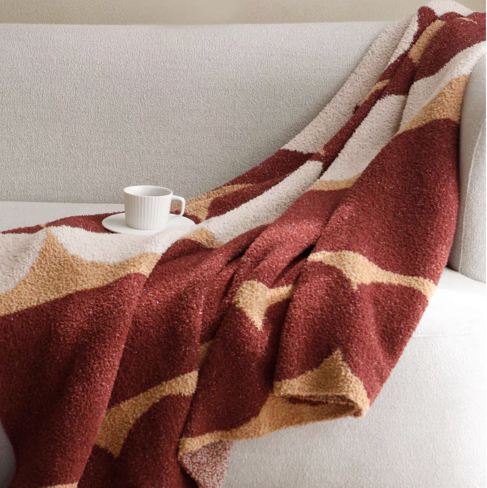 Red geometric circle throw blanket draped over sofa with cup, showing cozy plush texture and modern design