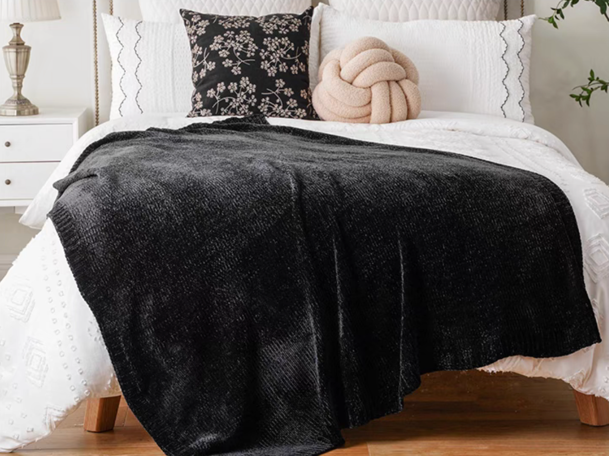 Black vertical rib chenille knit solid throw blanket draped across a white bed