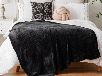 Black vertical rib chenille knit solid throw blanket draped across a white bed