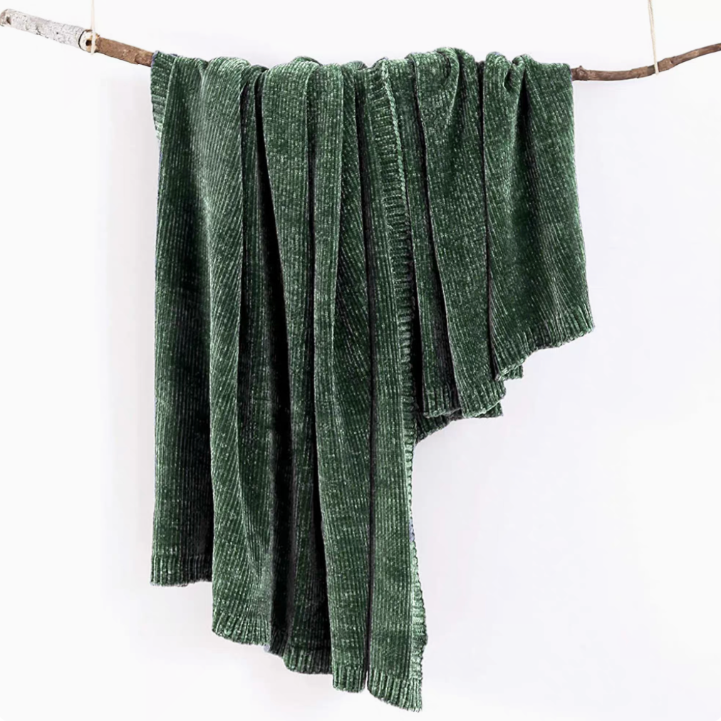 Forest green vertical rib chenille knit solid throw blanket hanging over a wooden branch