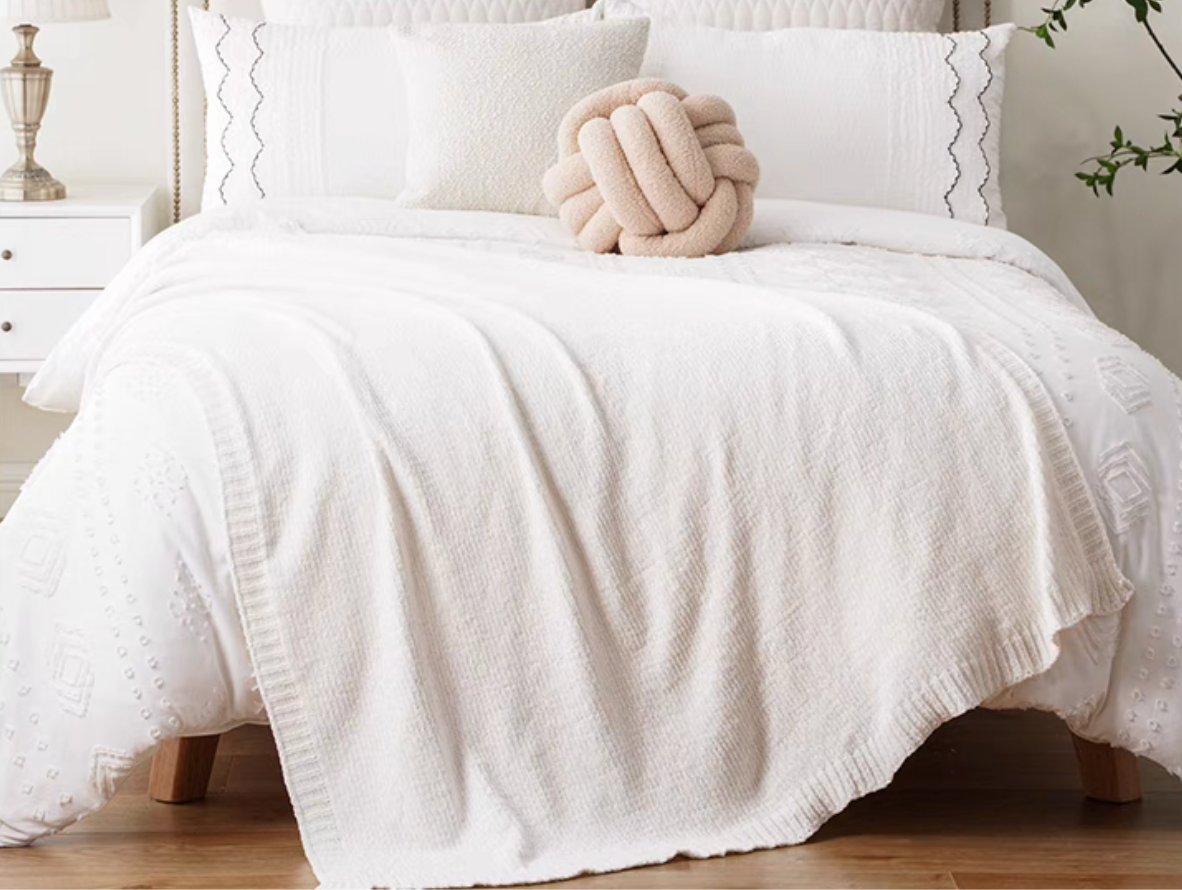 Ivory vertical rib chenille knit solid throw blanket draped across a white bed
