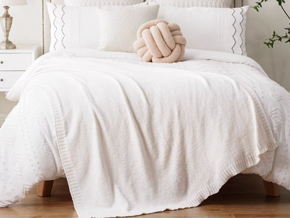 Ivory vertical rib chenille knit solid throw blanket draped across a white bed