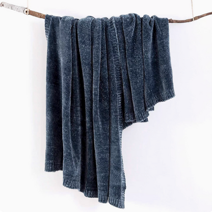 Navy blue vertical rib chenille knit solid throw blanket hanging over a wooden branch