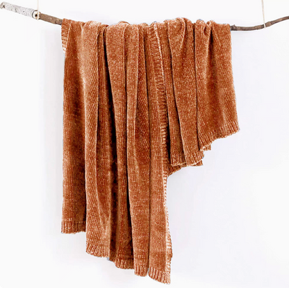 Orange vertical rib chenille knit solid throw blanket hanging over a wooden branch
