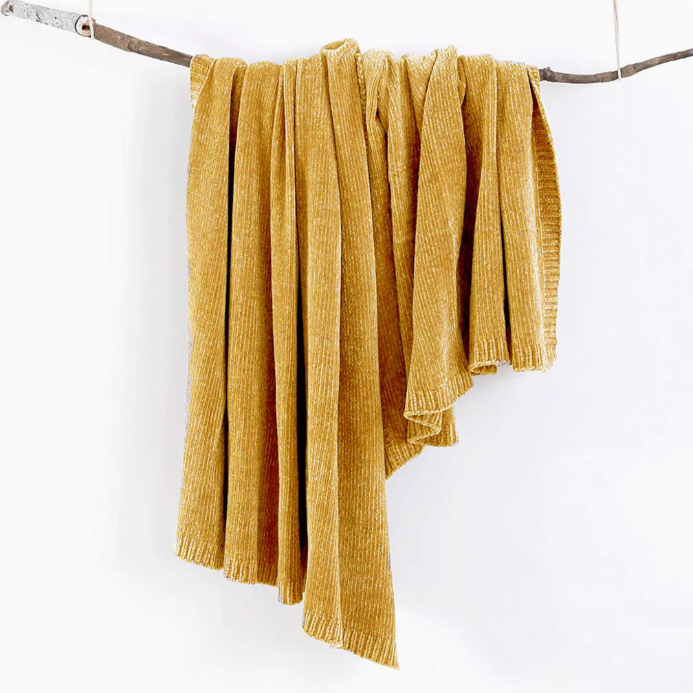 Yellow vertical rib chenille knit solid throw blanket hanging over a wooden branch