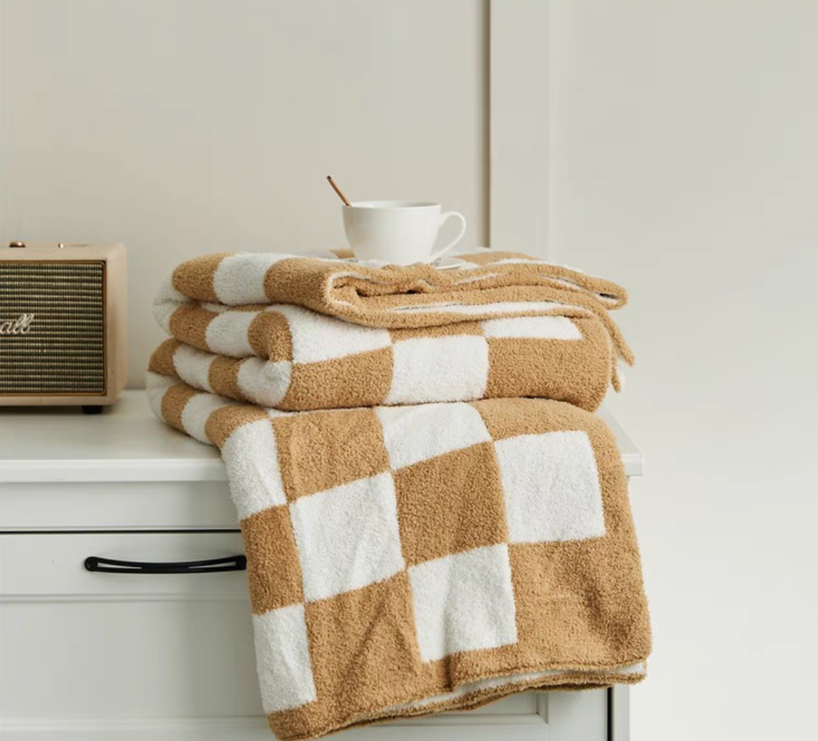 Light khaki checkered blanket folded neatly on drawer with coffee cup and retro speaker nearby
