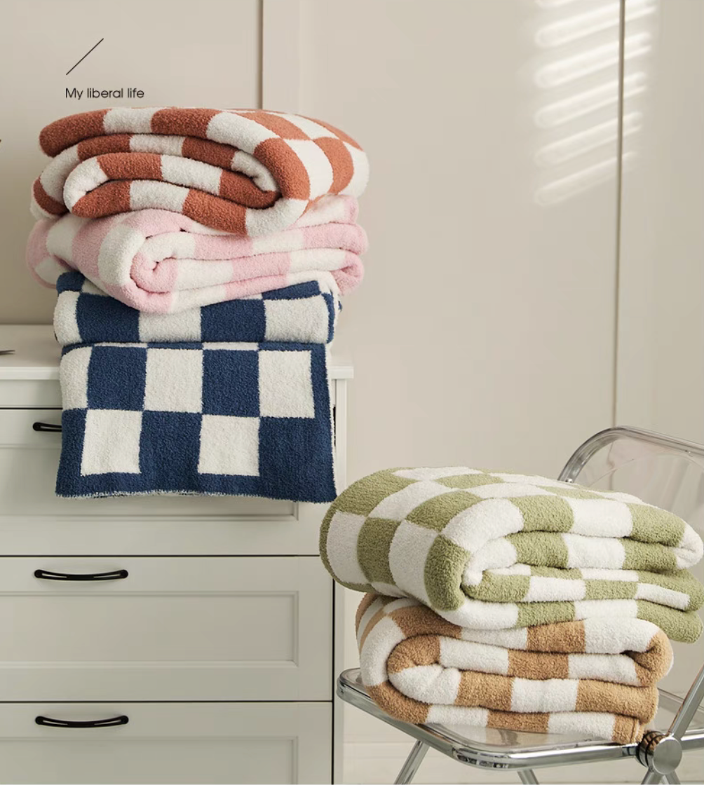 Stacked checkered blankets in navy, pink, rust, and matcha green folded on white drawer with soft natural light