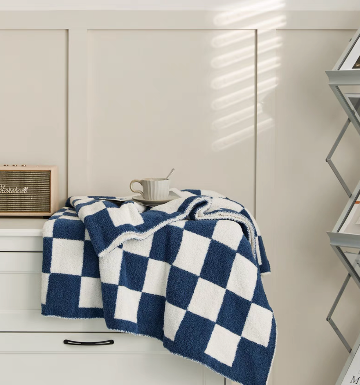 Navy blue checkered blanket draped over cabinet edge with white coffee cup on top in cozy indoor setting