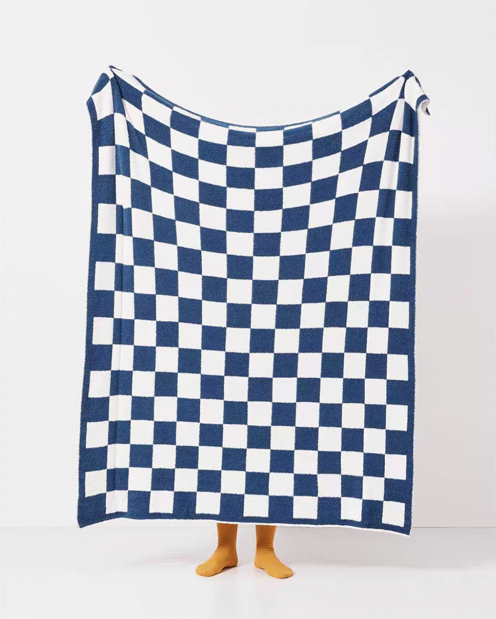 Navy blue and white checkered blanket fully extended in air showing complete checkerboard pattern with yellow socks visible below