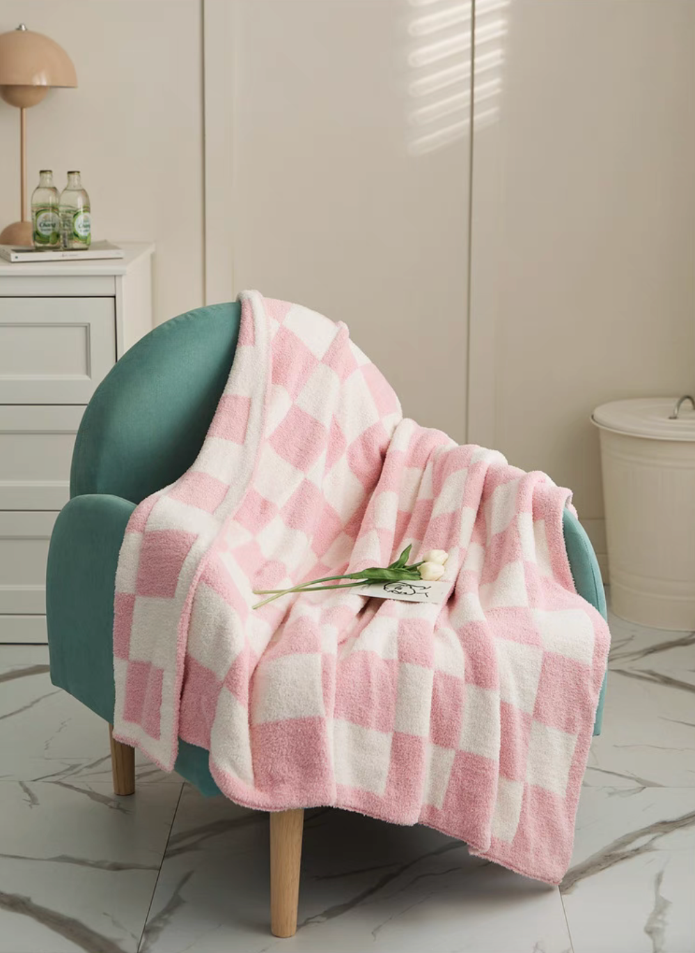 Pink checkered blanket draped over teal chair with small tulip decoration placed on fabric highlighting soft texture
