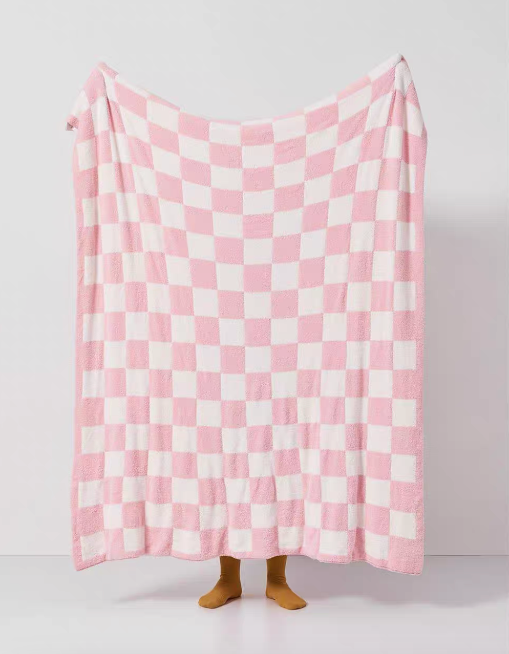 Pink and white checkered blanket fully spread in air revealing soft fuzzy surface and balanced checker pattern