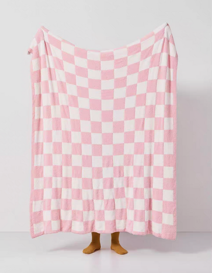 Pink and white checkered blanket fully spread in air revealing soft fuzzy surface and balanced checker pattern
