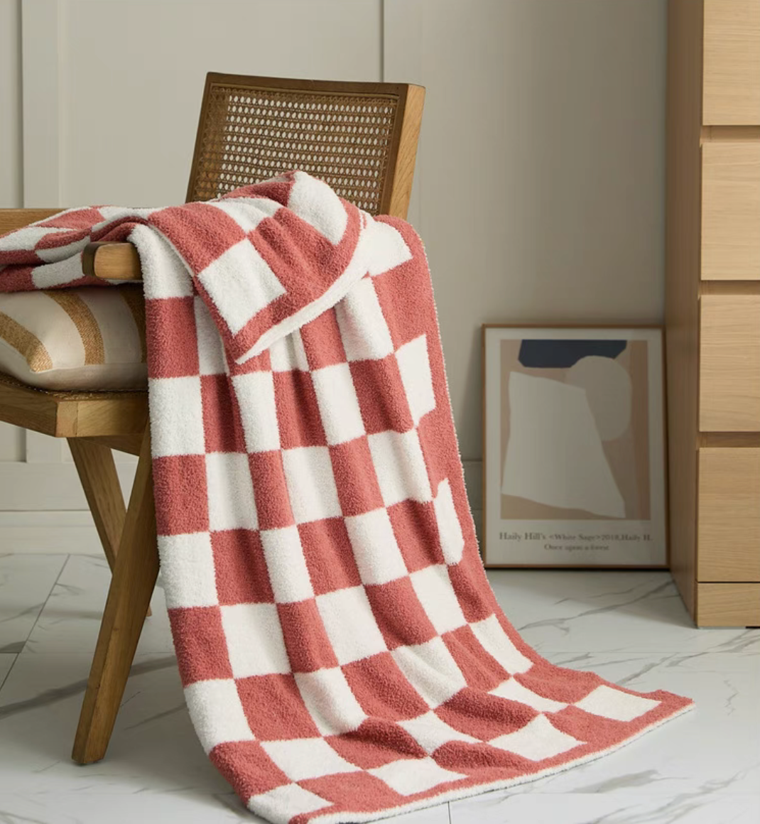 Watermelon red checkered blanket draped over wooden chair showing long flowing edge and soft texture