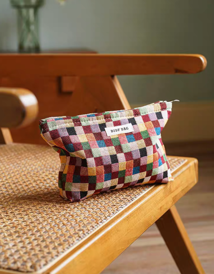 Large size Vibrant Checkered Travel Makeup Bag in multi-colored checkered pattern placed on woven chair in warm interior setting