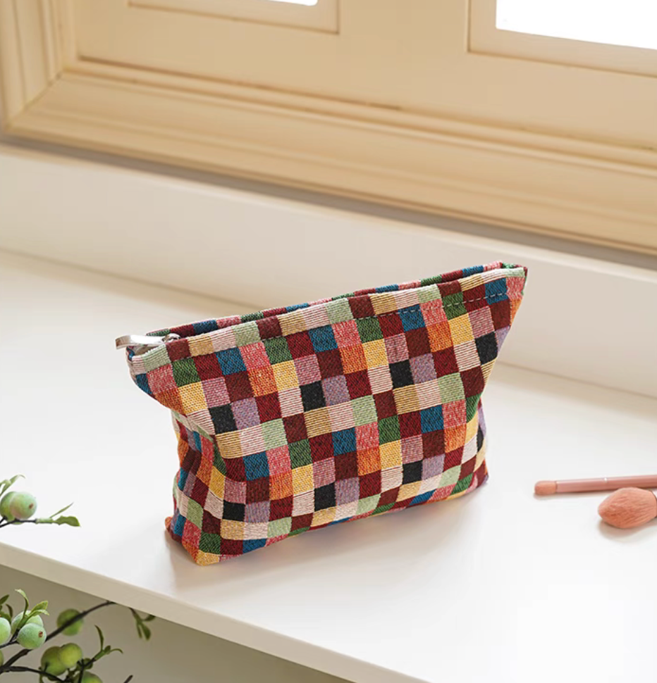 Large size Vibrant Checkered Travel Makeup Bag in multi-colored checkered pattern positioned on window ledge with makeup brush beside