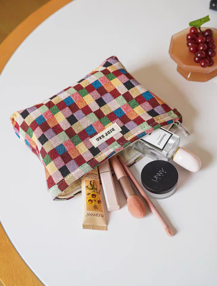 Small size Vibrant Checkered Travel Makeup Bag in multi-colored checkered pattern opened with cosmetics including brush, powder, and skincare items