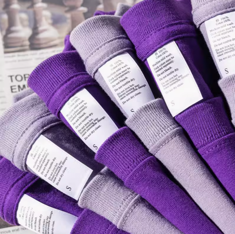Vibrant T-Shirt Collection light purple and dark purple stacked shirts with visible care labels showing cotton fabric details