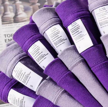 Vibrant T-Shirt Collection light purple and dark purple stacked shirts with visible care labels showing cotton fabric details