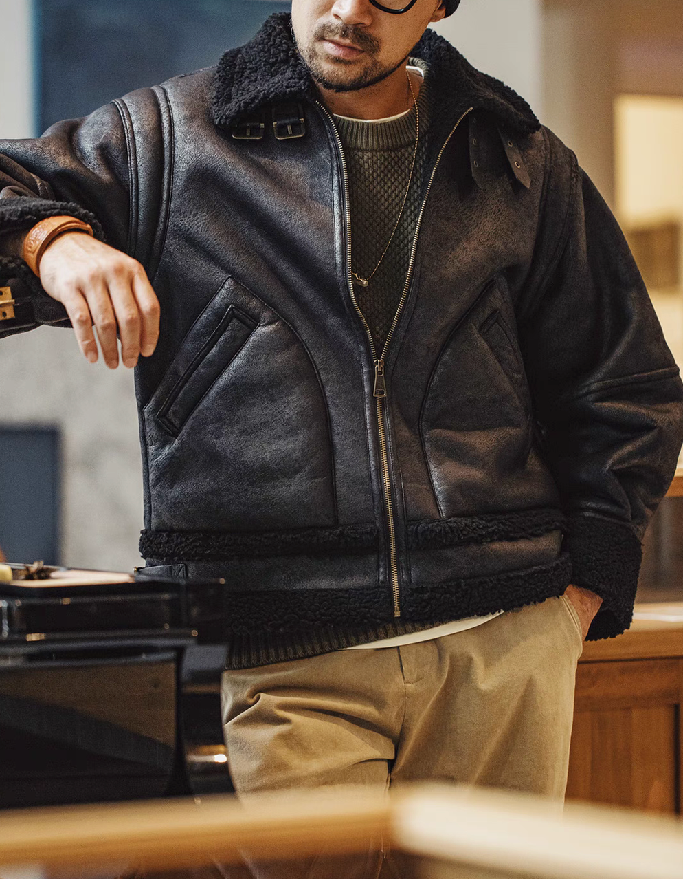 Man wearing Vintage-Inspired Faux Sherpa B3 Bomber Jacket in Black with zip front closure sherpa collar and casual indoor styling
