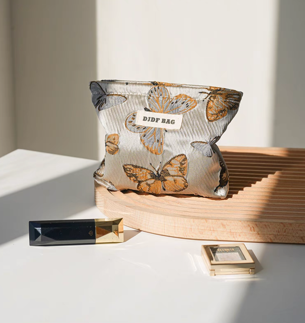 Vintage Butterfly Pattern Portable Makeup Bag in vintage butterfly print placed on round wooden platform with cosmetics beside