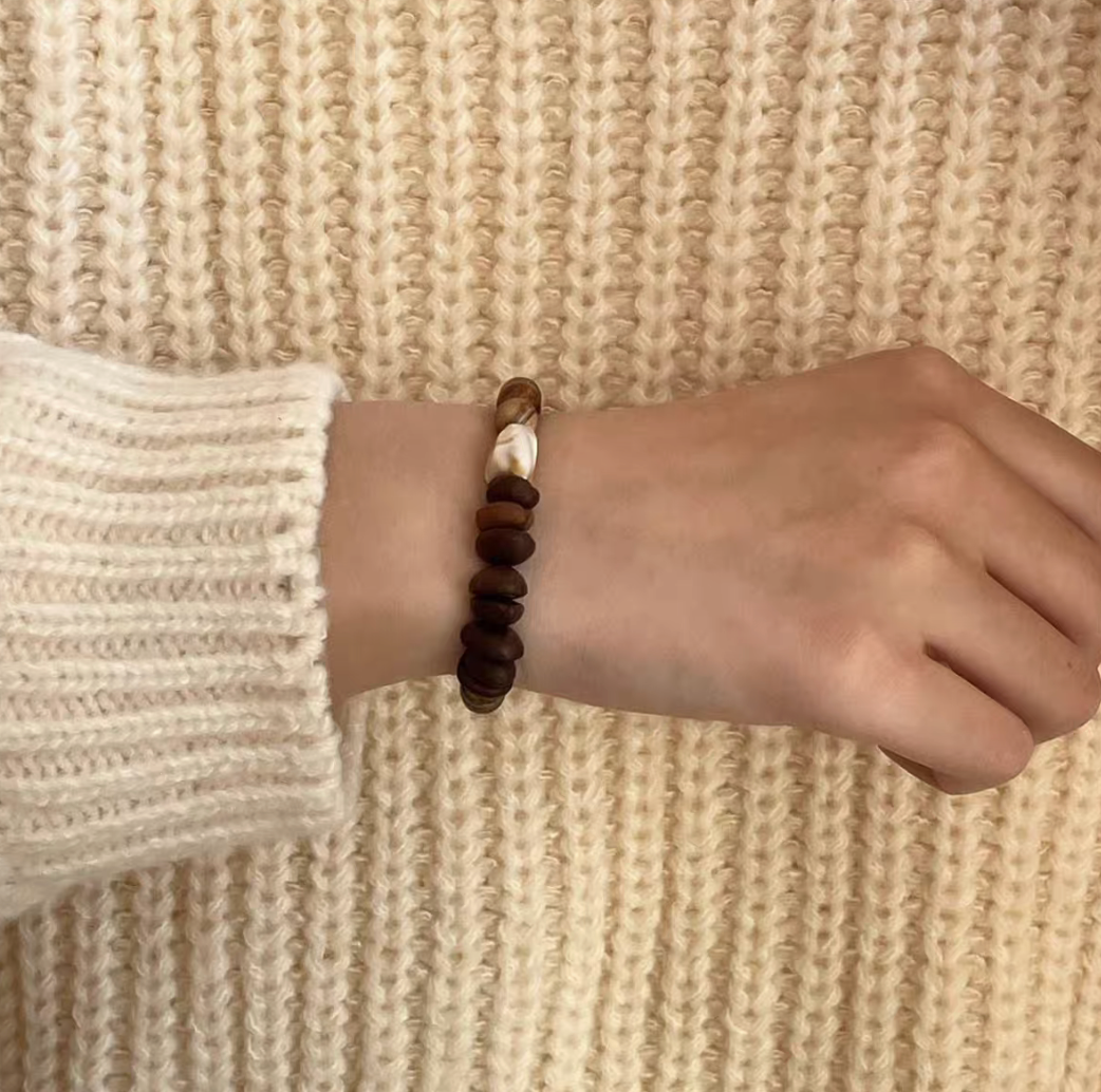 Vintage coffee bean and wood bracelet worn on wrist with cream knit sweater highlighting layered wood beads coconut shell and coffee bean detail